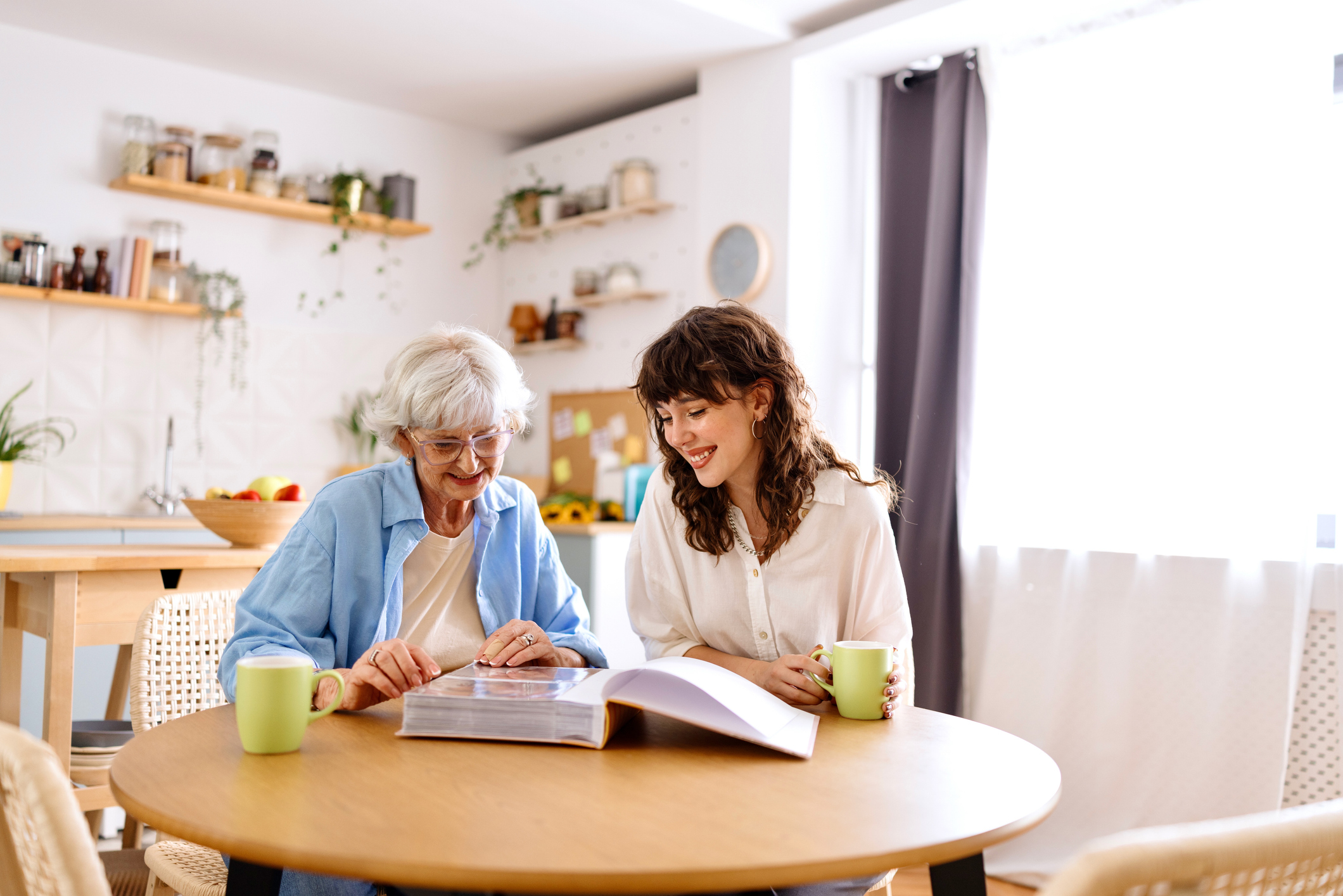 Senior woman and her grandchild looking at the old photo album while sitting in the dining room