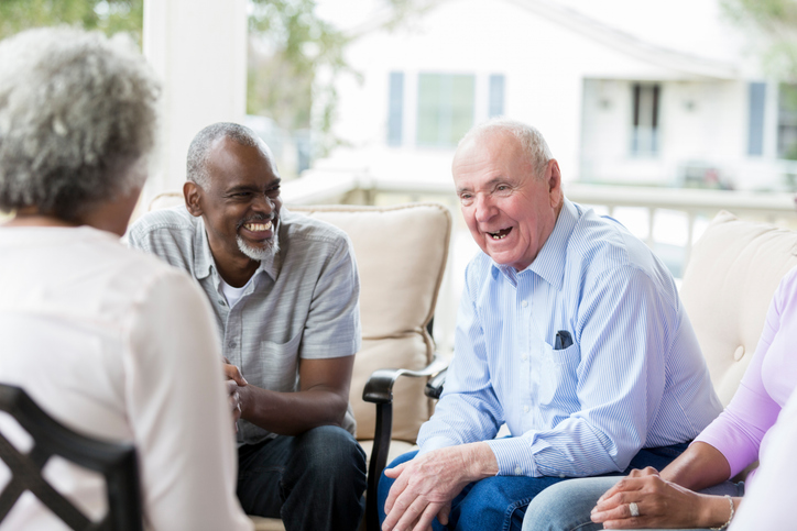 Cheerful senior man tells his friends a story from his childhood. They are attentively listening to the man tell a story.